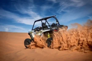 Tourists driving dune buggies across the vast, golden desert landscape of Dubai under a clear sky, enjoying an adventurous and affordable experience.