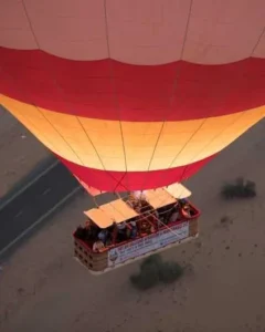 Private hot air balloon with two people in the basket floating over the Dubai desert at sunrise, with the city skyline in the distance